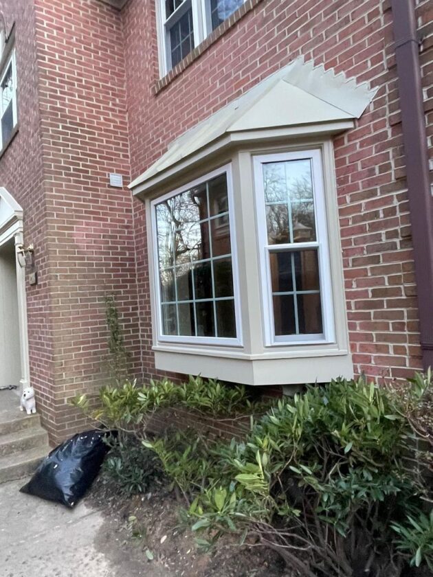 A new triple-pane window installed on a red brick townhome with an awning above and shrubs below