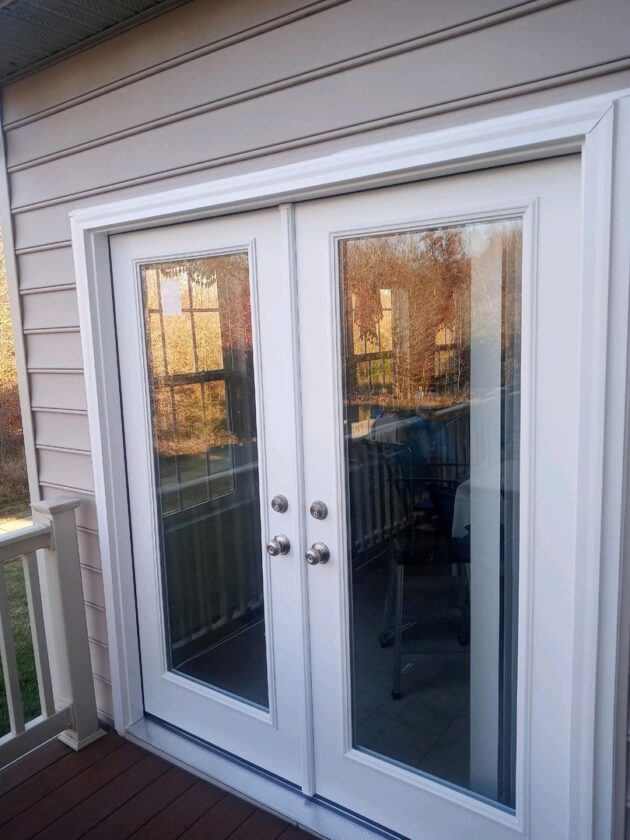 White French doors with reflective glass installed on a home's deck, with a suburban backyard visible in the reflection