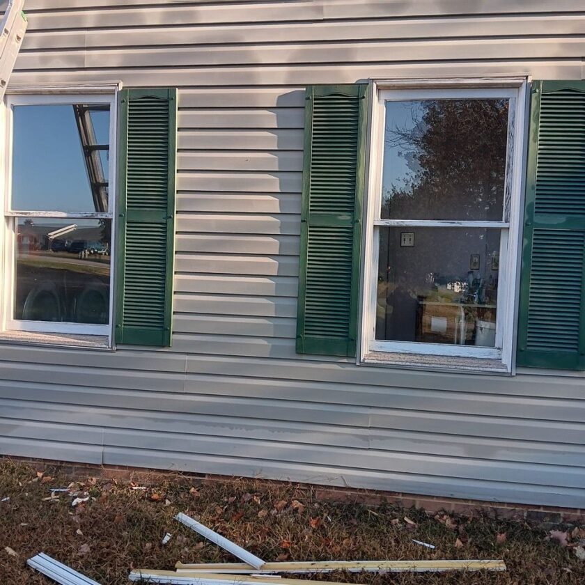House with vinyl siding and new windows with green shutters, and old window materials on the ground