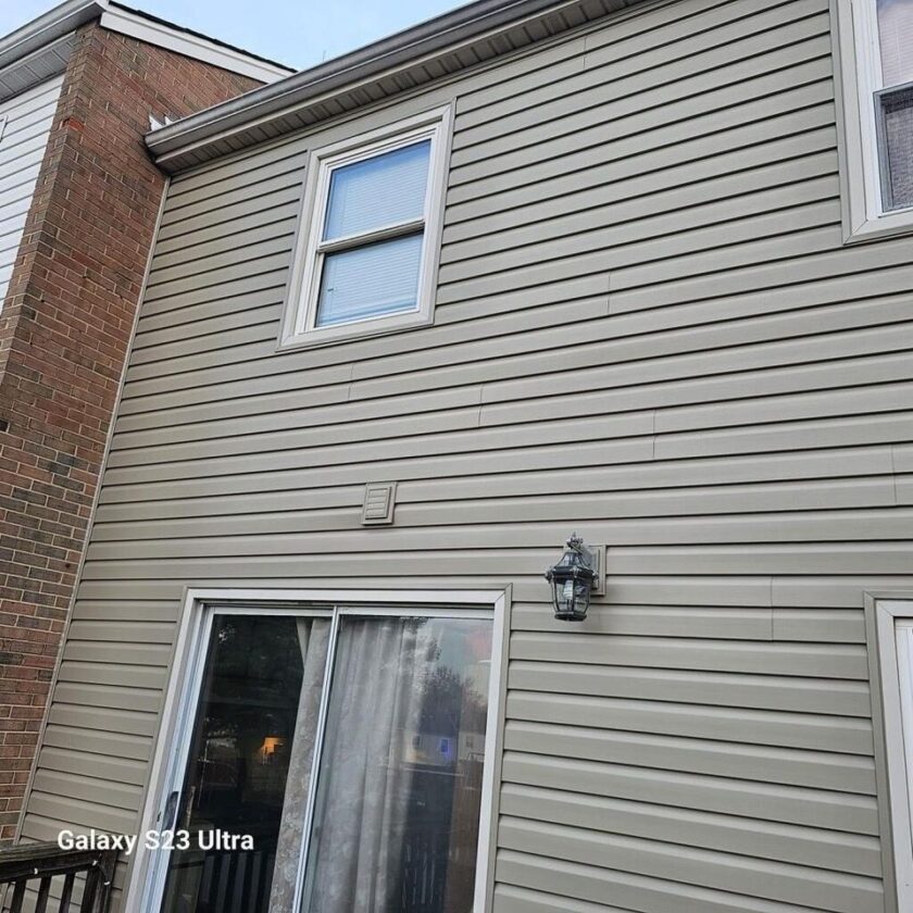 Exterior view of a townhouse with new beige vinyl siding, a window, and a sliding door