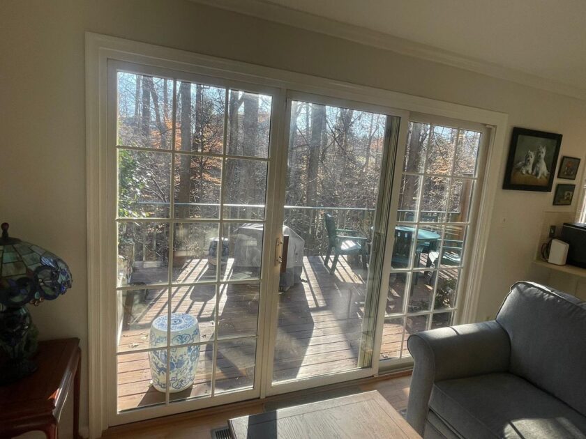 Interior view of a room with a large sliding glass door leading to a sunny deck surrounded by trees