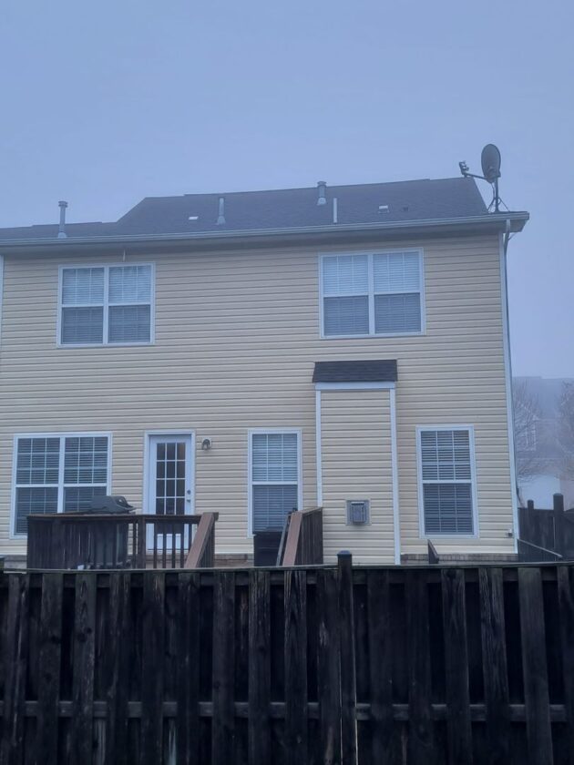 Image of a two-story house with beige siding and a wooden fence in misty weather