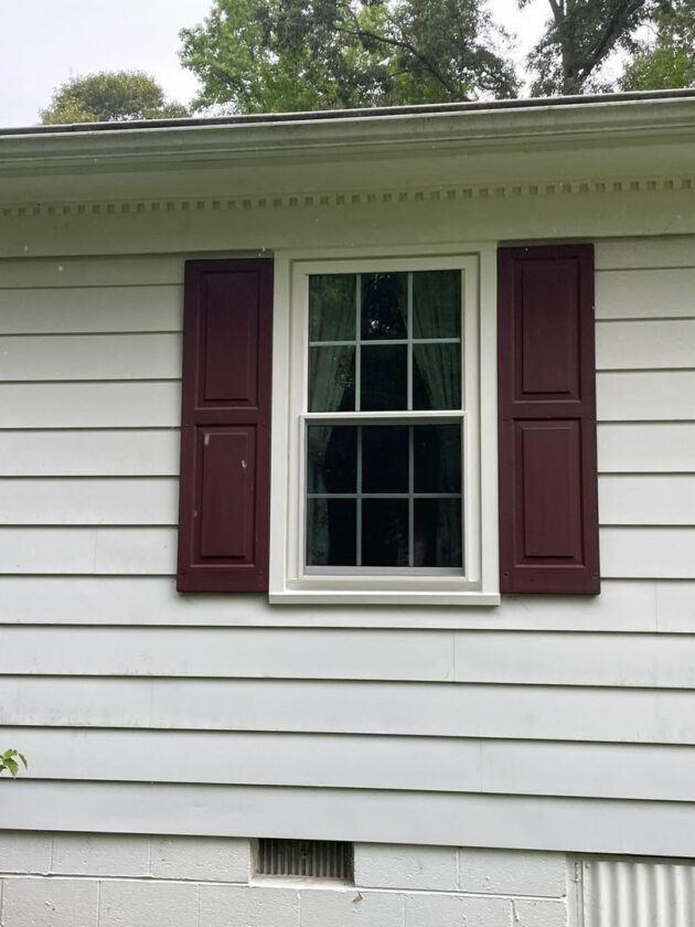 A new white double-hung window with red shutters on a house with white siding