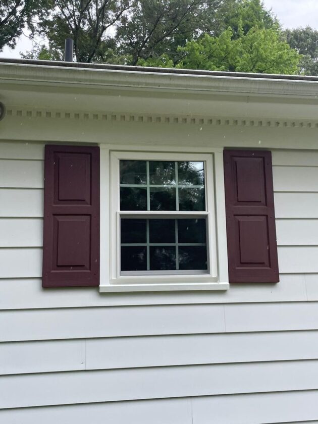 A new six-pane double-hung window with dark shutters on a house with light-colored siding