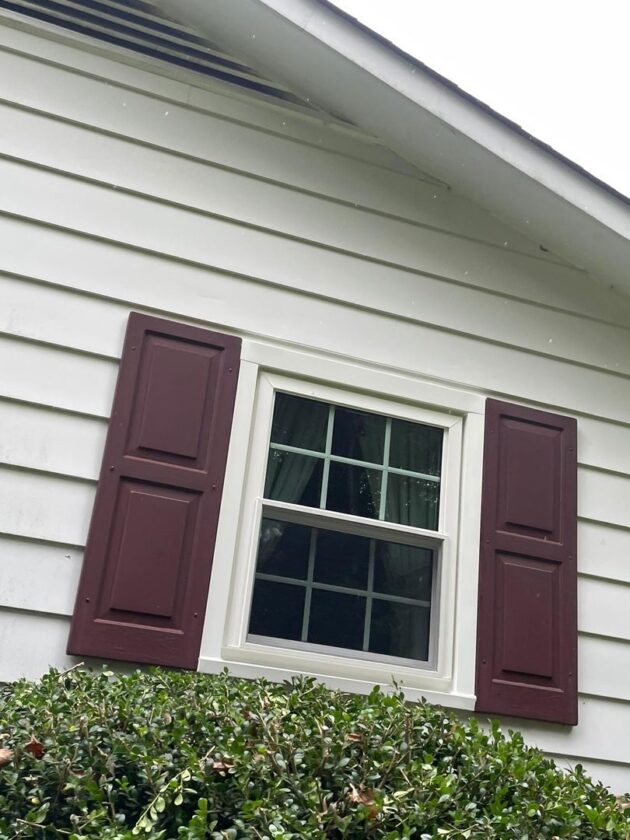 Double-hung window with six panes each in upper and lower sashes, flanked by maroon shutters on a white siding house wall
