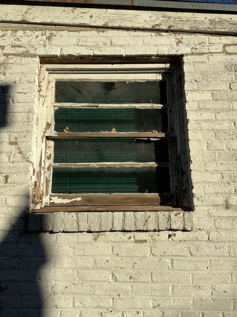 Old wooden window with peeling paint and broken panes in a white brick wall