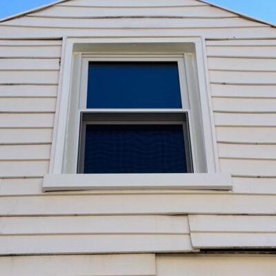 A new triple pane window installed in the upper story of a light beige house with clear blue sky in the background