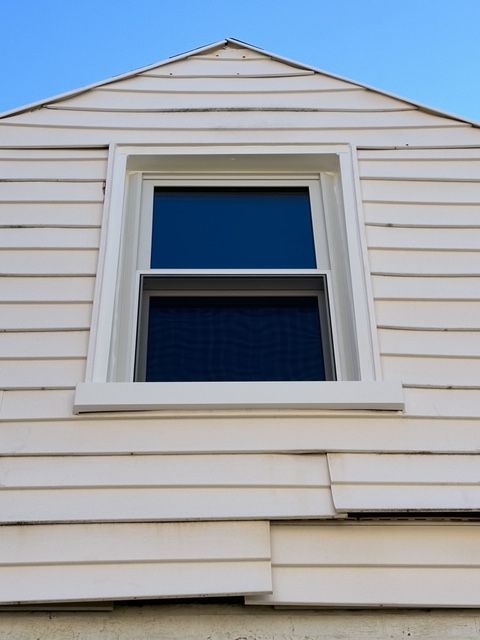 A new triple pane window installed in the upper story of a light beige house with clear blue sky in the background