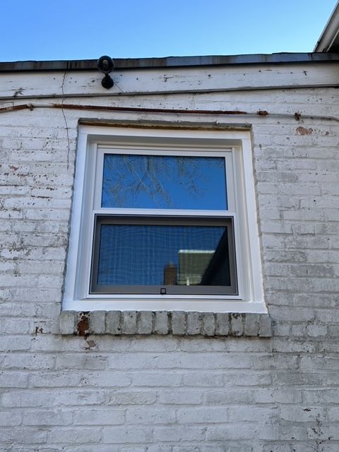 A new white-framed triple pane window installed in an old white brick wall with a security camera above it