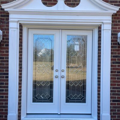 White French doors with decorative glass and sidelights on a brick house with a welcome mat