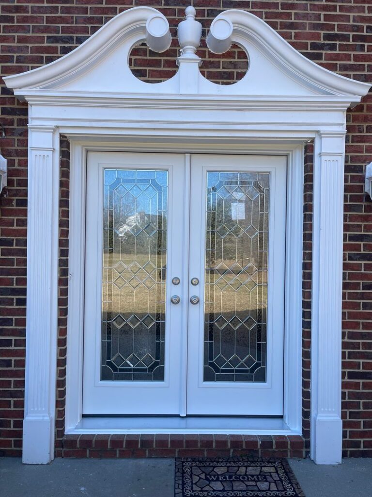 White French doors with decorative glass and sidelights on a brick house with a welcome mat