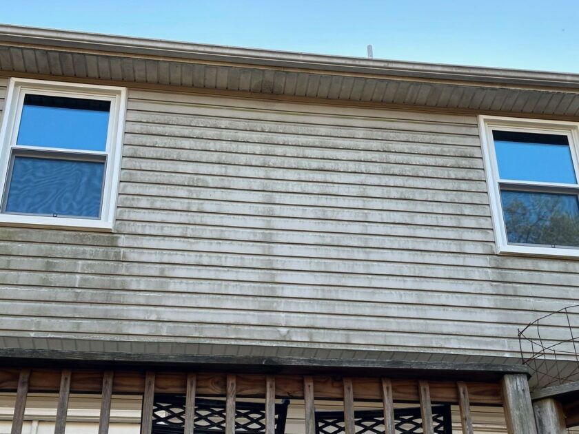 Upper level of a house with two new windows and dirty, streaked siding