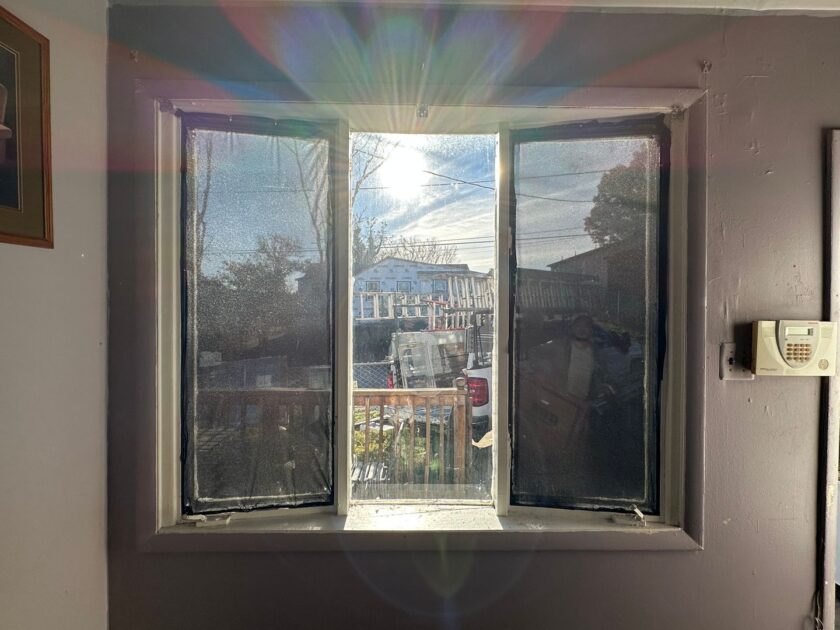 Interior view of a triple-pane window with sunlight flares and a view of the neighborhood outside