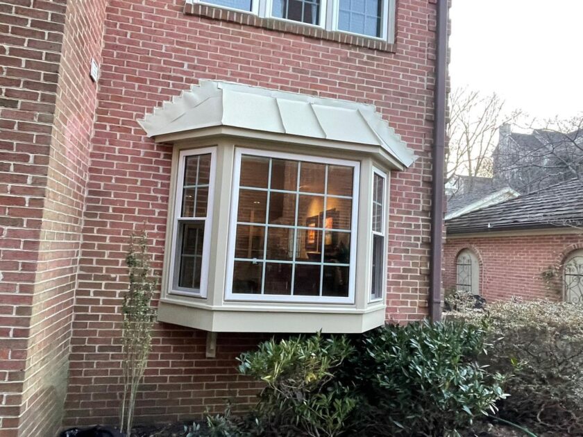 A new bay window with a cream frame installed on a red brick residential building at dusk