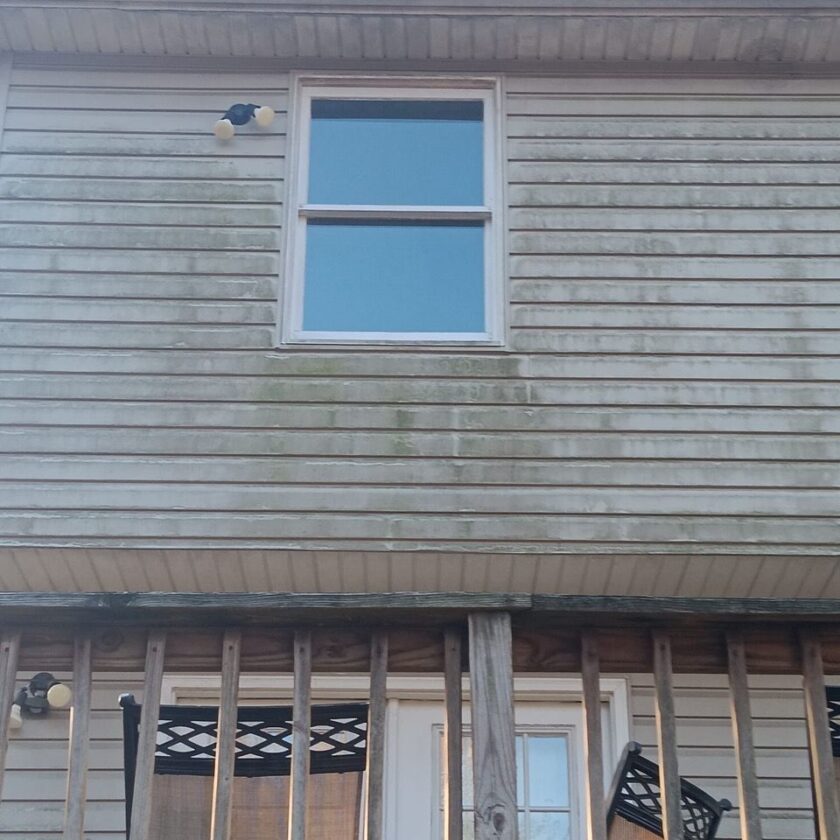 Close-up of a house's weathered siding with a single window and algae growth